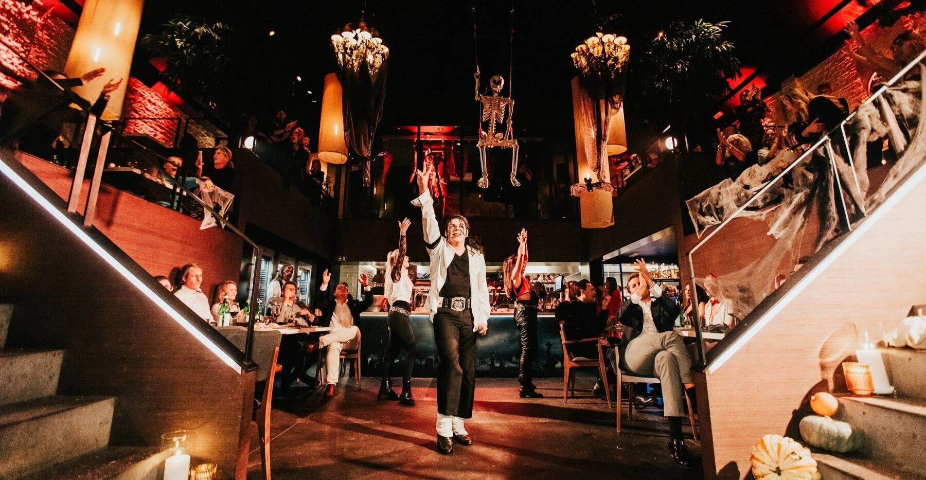 Een Michael Jackson-imitator danst tussen de tafels, boven hem schommelt een skelet.