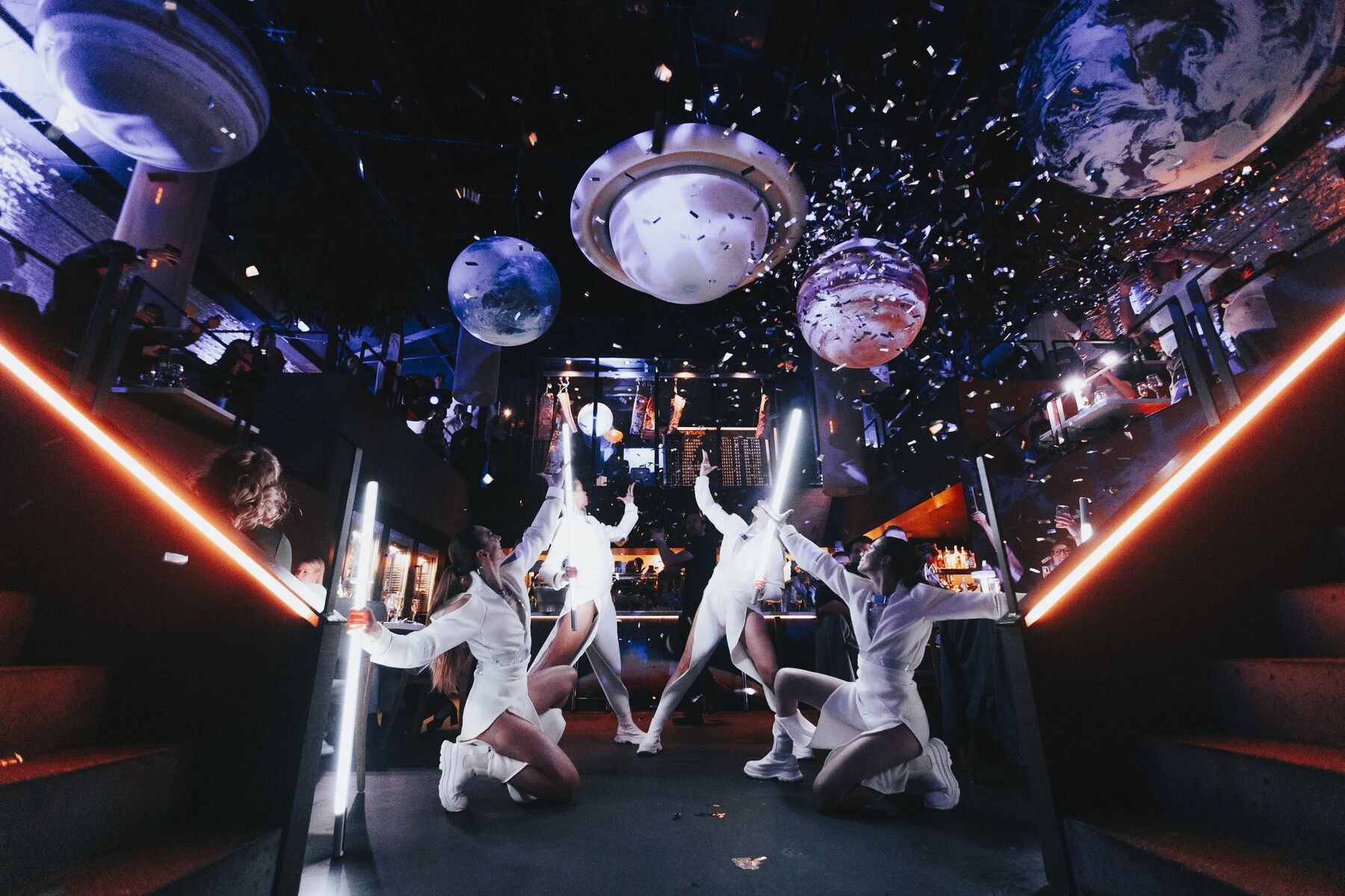Planeten boven de zaal, confetti, dansers in witte ruimtepakken.